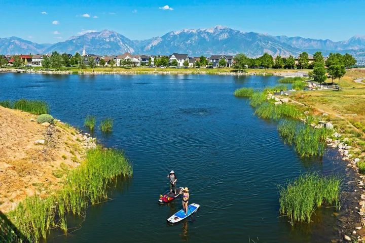 Expansive body of water with natural vegetation, bordered by developed land with residential structures, and a distant mountain range