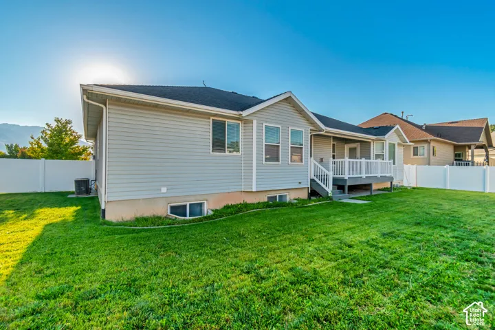 Expansive backyard featuring a manicured lawn, a white privacy fence, and a raised exterior deck with white railings