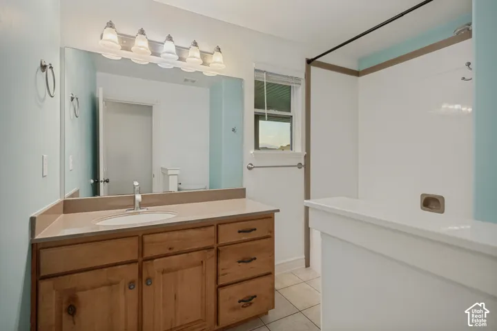 Master bathroom featuring a wood-finish vanity with dual sink configuration, ceramic tile flooring, and a spacious walk-in shower with glass enclosure and tile surround