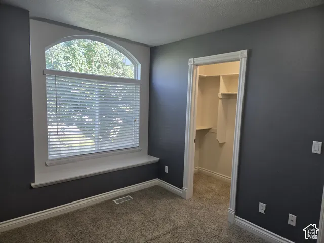 Arched window with integrated blinds, built-in window sill, plush carpet flooring, crisp white trim, and a functional closet with shelving