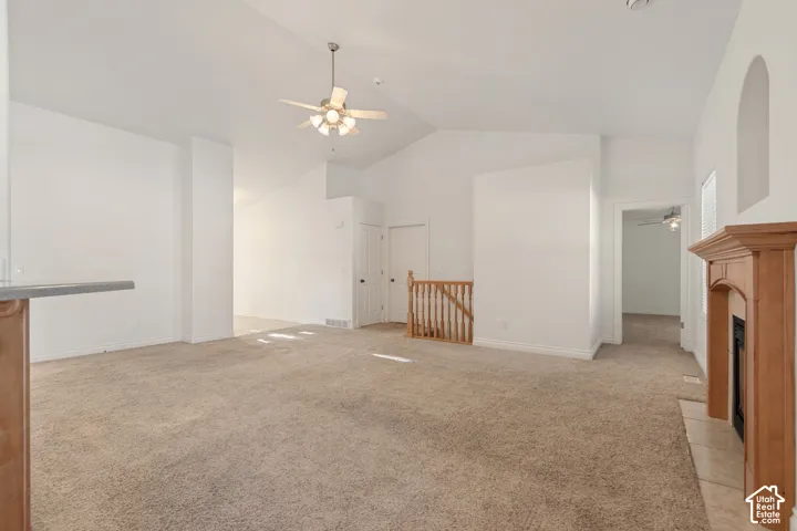 Vaulted ceilings, a ceiling fan with integrated lighting, a wood-finish fireplace mantel with tile surround, and a wood banister