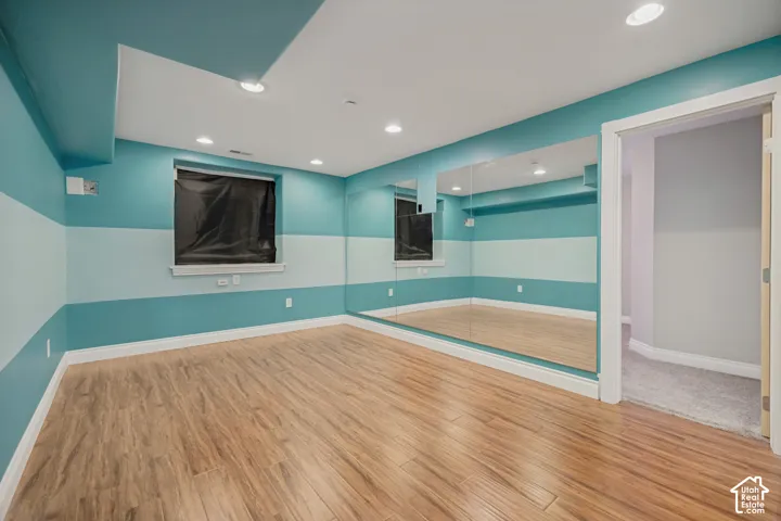 Wood-finish flooring, recessed lighting, floor-to-ceiling mirrored wall, and a window with a sill