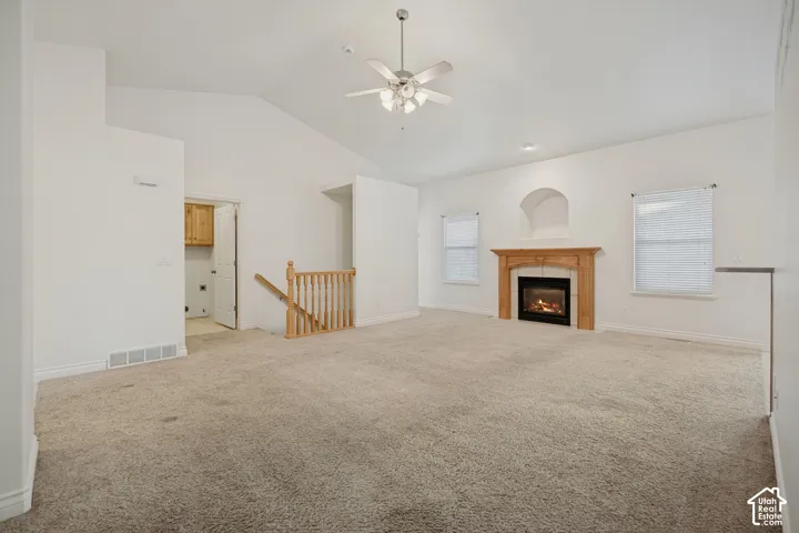 Vaulted ceiling with a ceiling fan, fireplace with a wood-finish mantel, built-in wall niche, and natural wood-finish stair railing