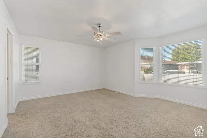 Recessed bay window, ceiling fan with integrated lighting, textured carpeting, and multiple windows with blinds