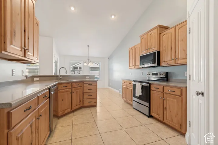Kitchen featuring wood cabinetry, stainless steel appliances, tile flooring, and vaulted ceiling with recessed lighting