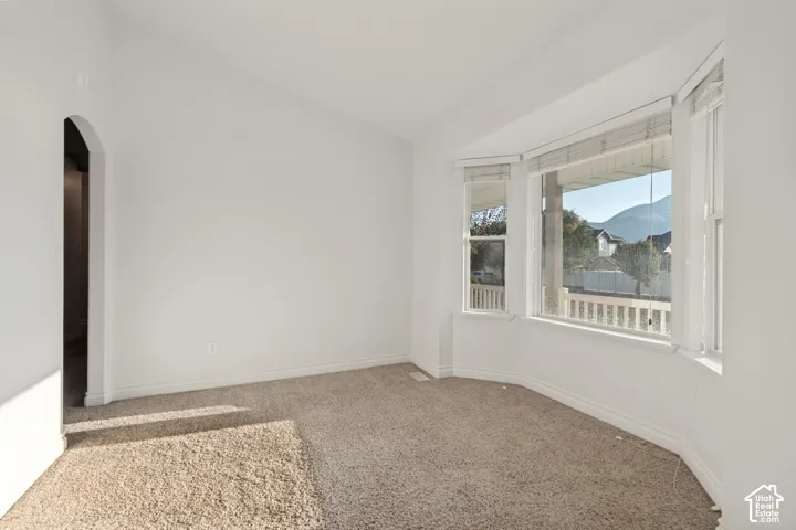 Arched doorway, vaulted ceiling, bay window, light-colored carpeting, and neutral wall tones