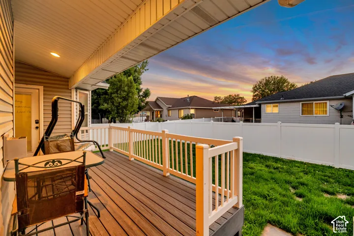 Covered outdoor deck with wood-finish flooring, white railing, and an adjacent green space