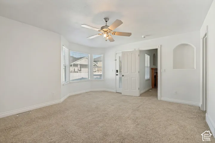 Bay window with horizontal blinds, ceiling fan with light fixture, neutral carpet flooring, arched wall niche, and double French doors with glass panels