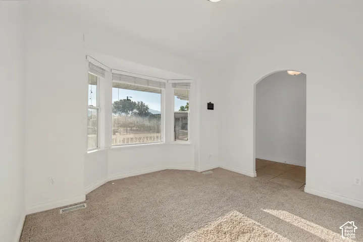 Bay window with multiple panels, carpeted flooring, and an arched entryway to a tiled space