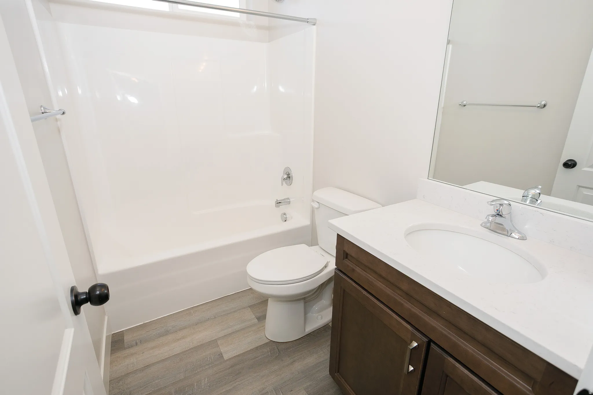 White bathtub with shower, white toilet, wood-finish flooring, vanity with white countertop, and dark wood-finish cabinetry
