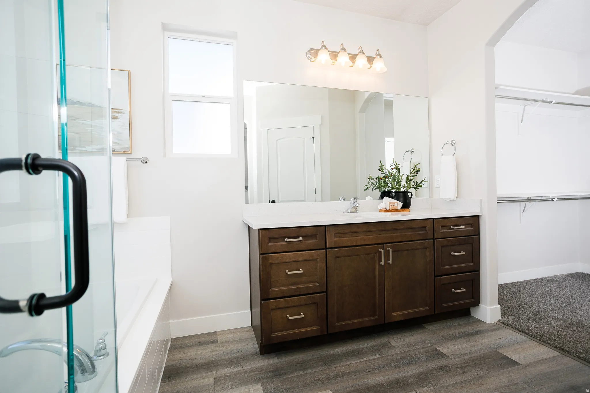 Wood-finish flooring with a glass-enclosed shower, built-in tub, and a vanity with a white countertop