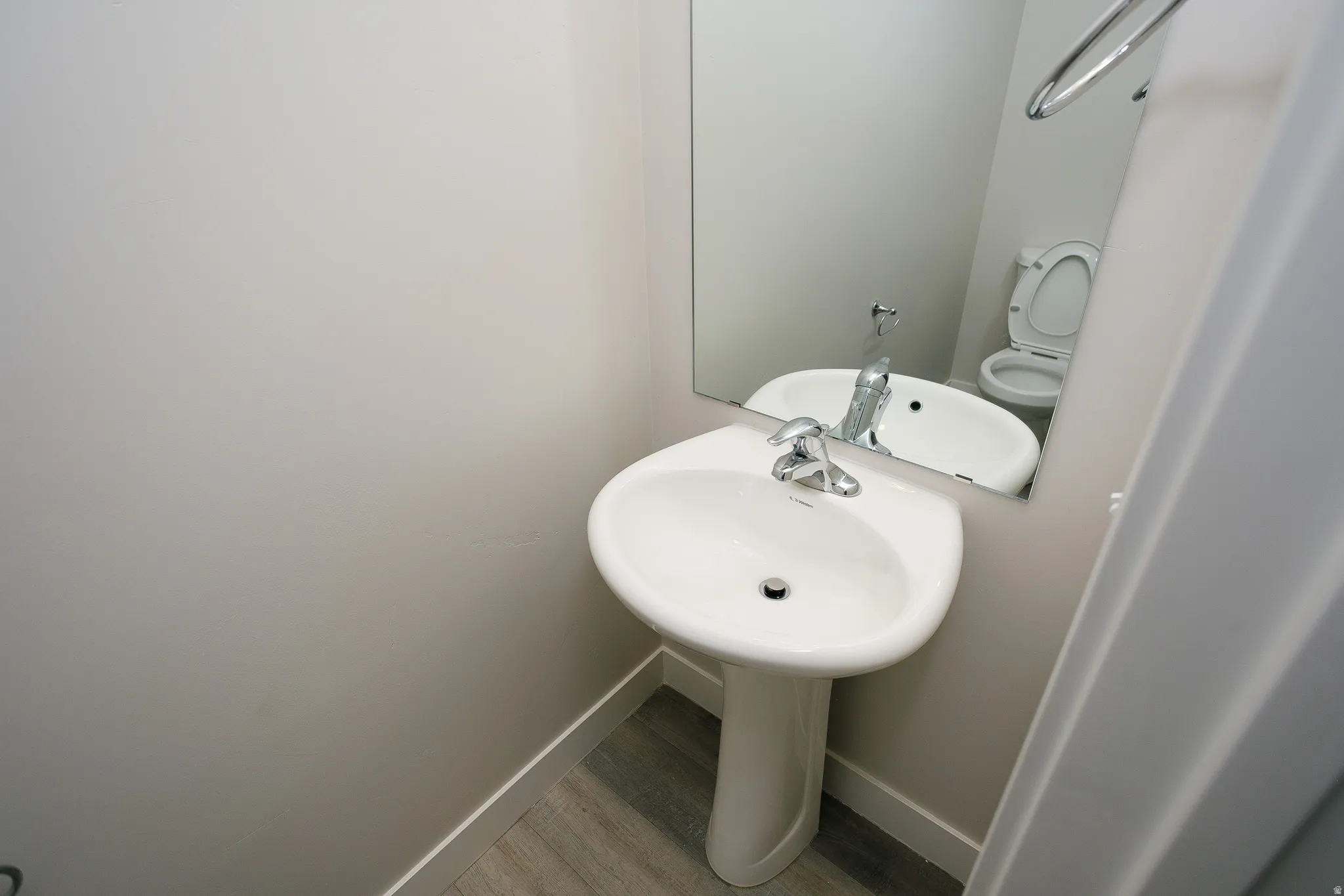 Pedestal sink, wall-mounted mirror, chrome single-handle faucet, wood-finish flooring, and light gray walls