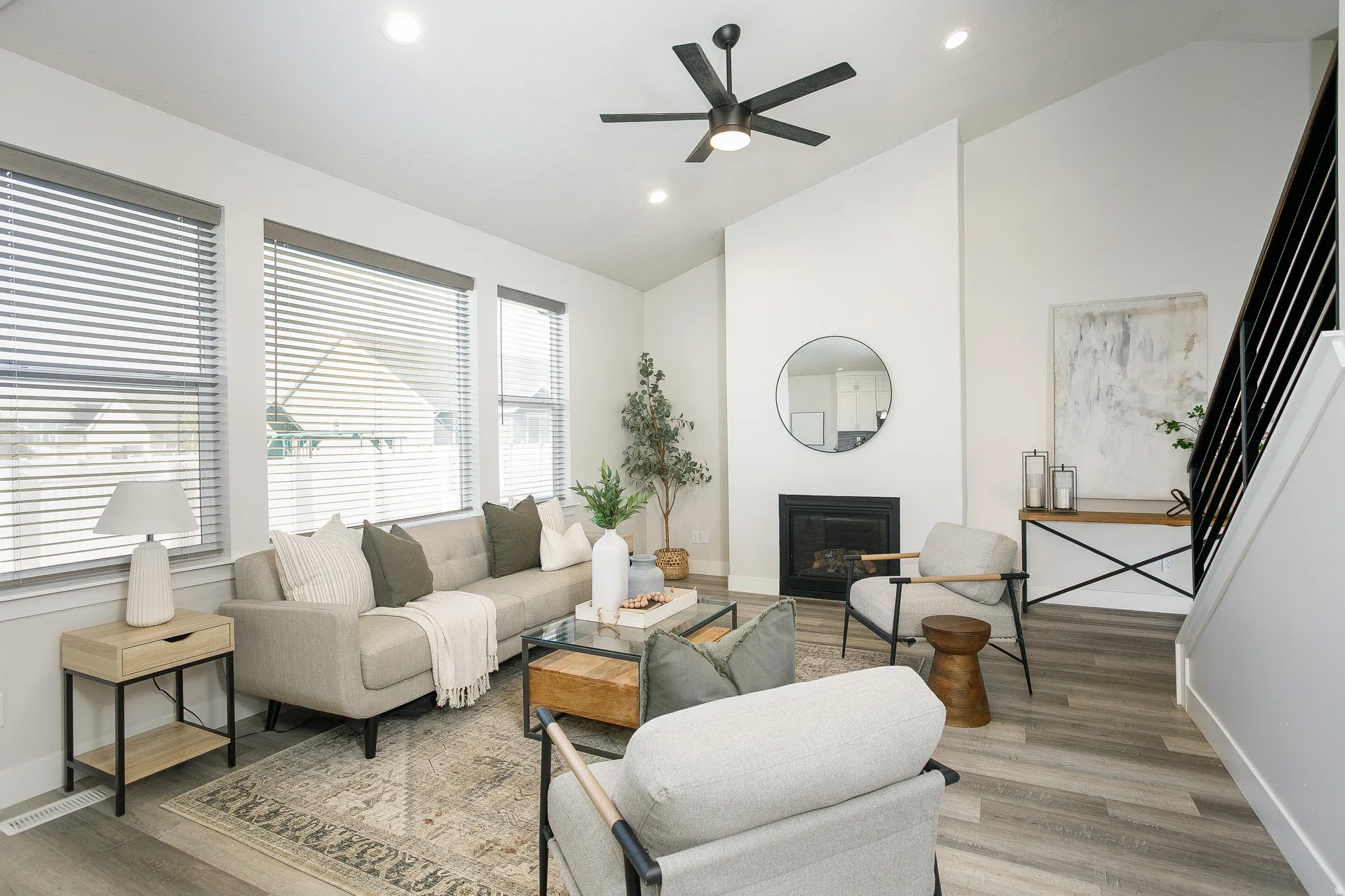 Bright, open living area featuring a ceiling fan, recessed lighting, and large multi-pane windows with horizontal blinds