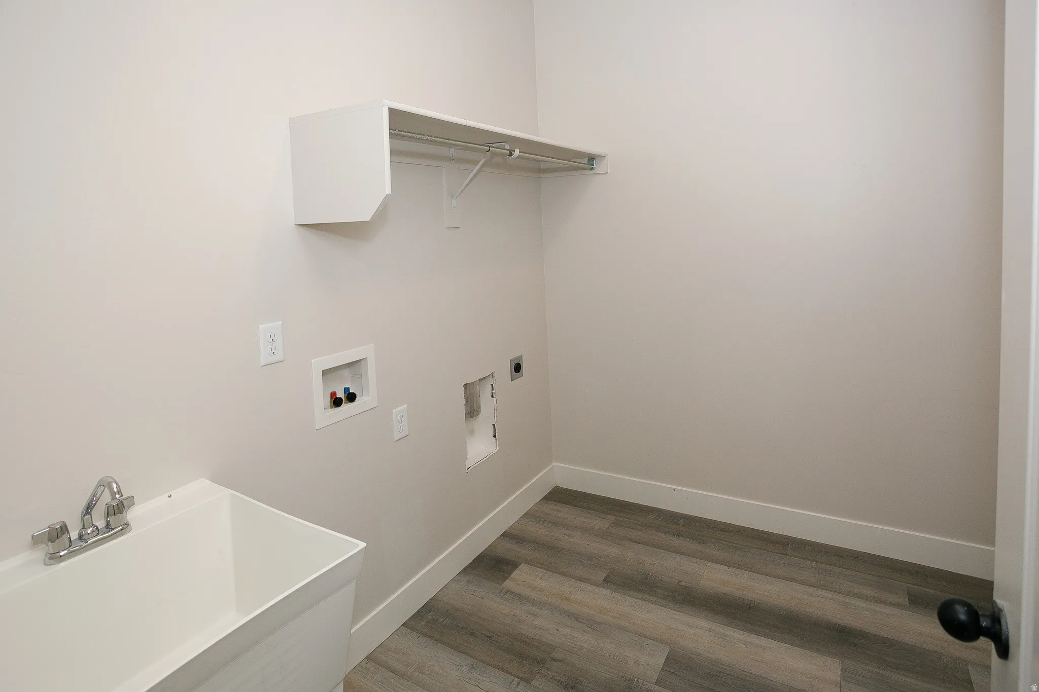 Utility space featuring wood-finish flooring, a utility sink with a chrome faucet, and an overhead shelf with a hanging rod