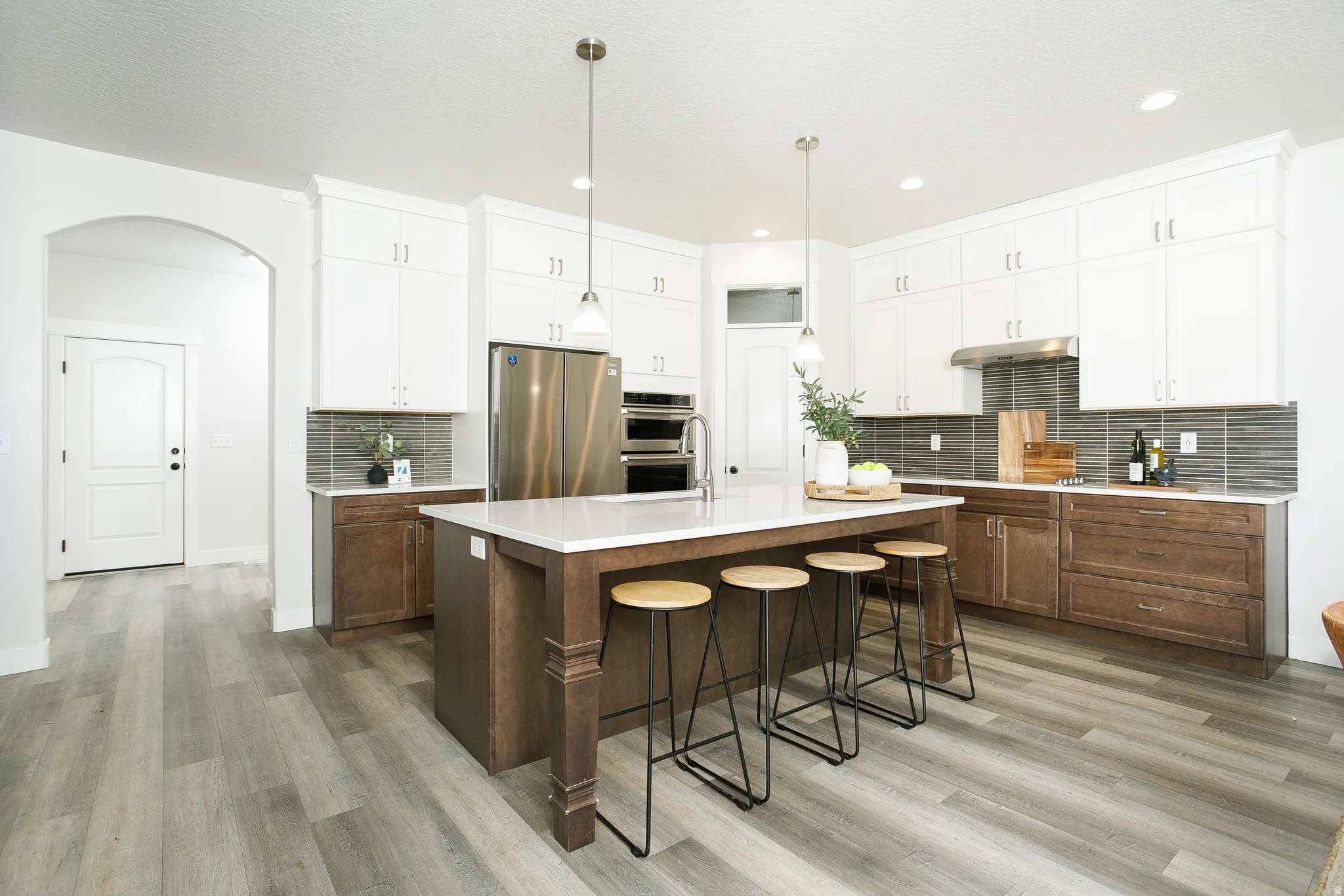 Kitchen featuring an expansive island with seating, stainless steel appliances, two-tone cabinetry, a tile backsplash, and light wood-finish flooring