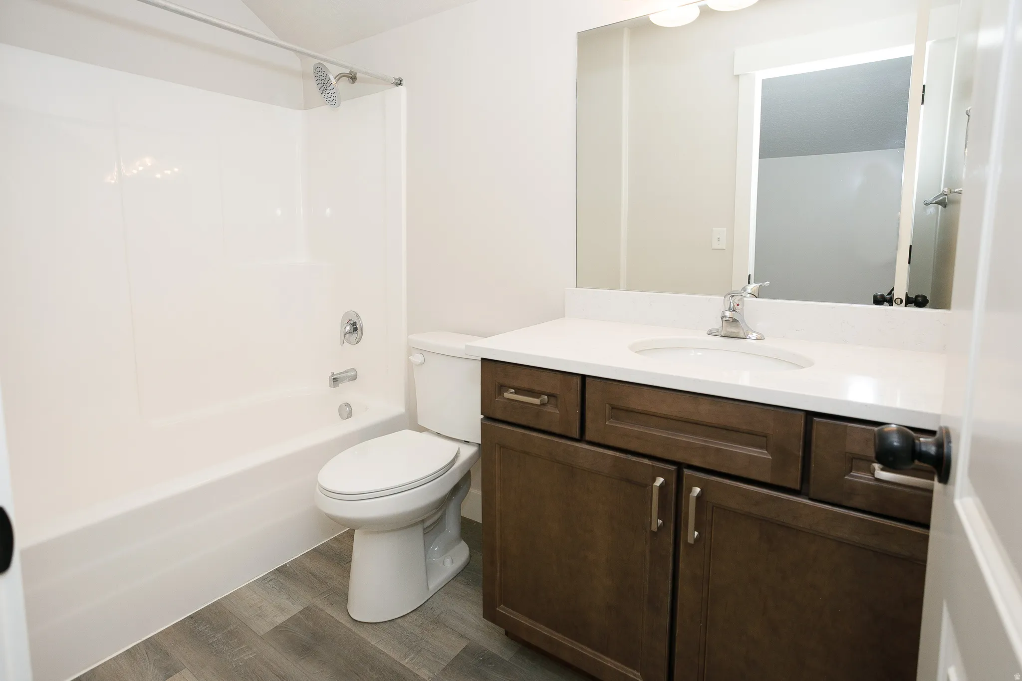 White bathtub and shower combination, wood-finish flooring, dark wood-finish vanity with drawer and cabinet storage, white countertop, and an integrated mirror