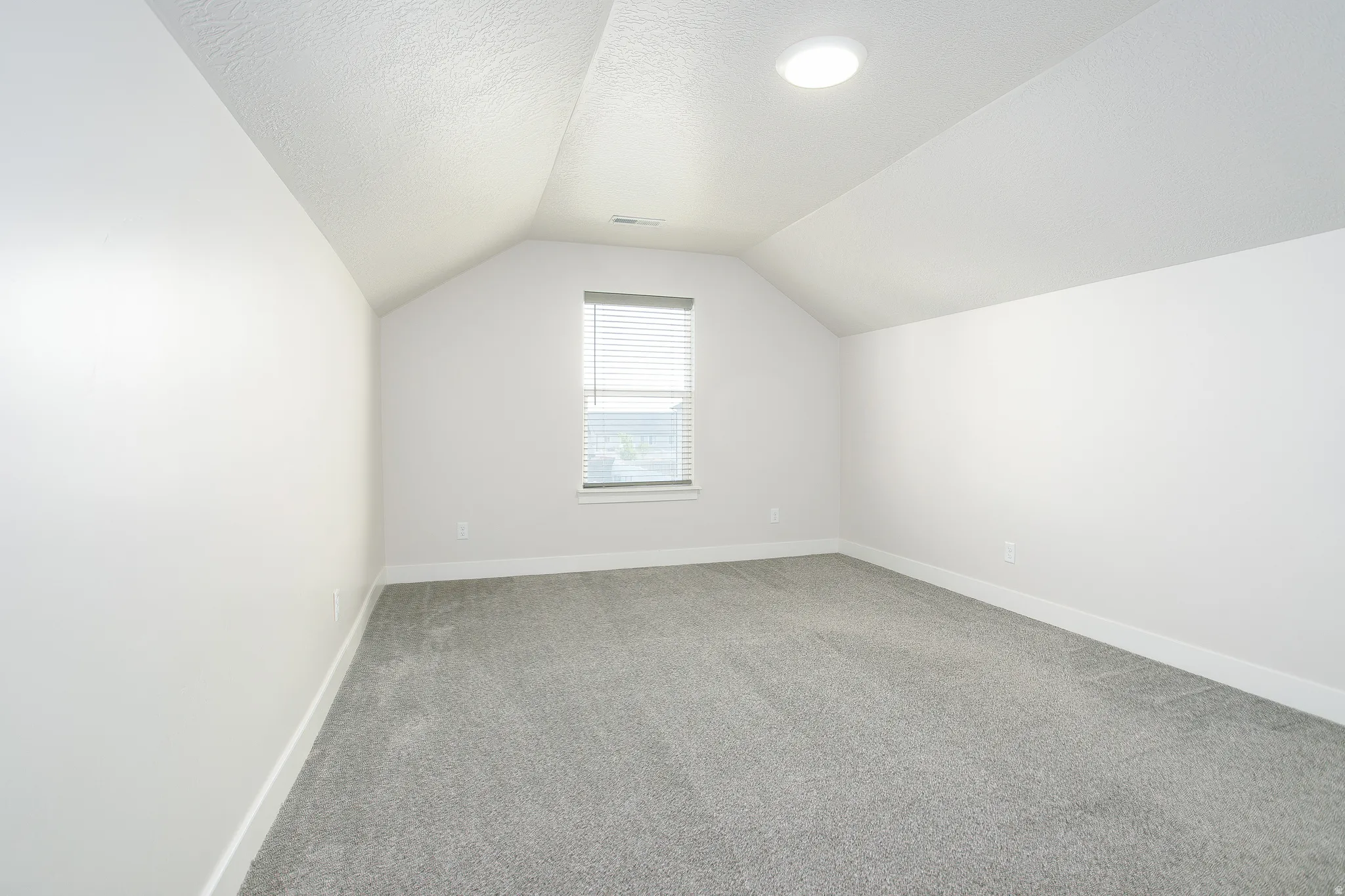 Vaulted ceiling with recessed lighting, gray carpeting, white walls, and a window with blinds