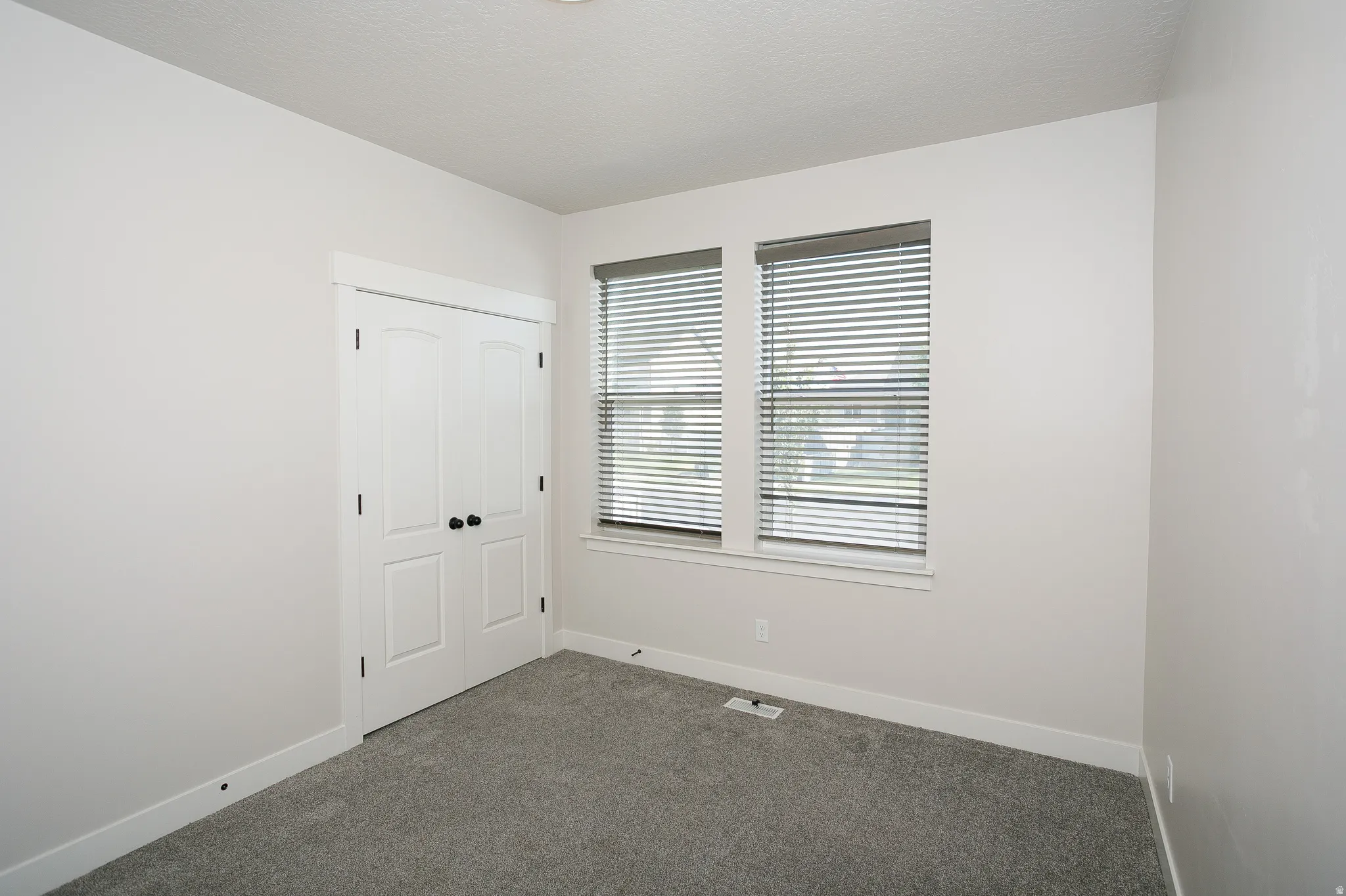 White paneled bi-fold closet doors, carpeted flooring, and two windows with blinds