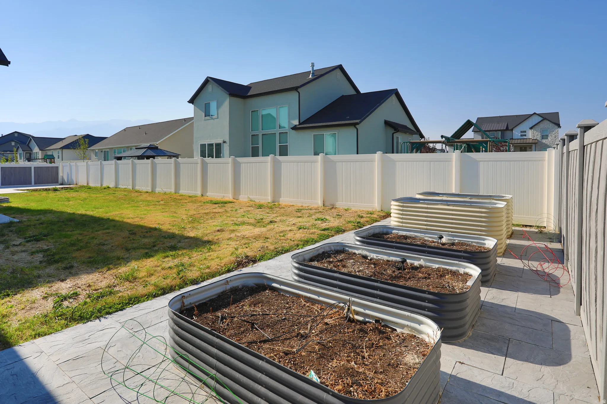 Expansive backyard featuring a privacy fence, concrete patio, and multiple raised garden beds