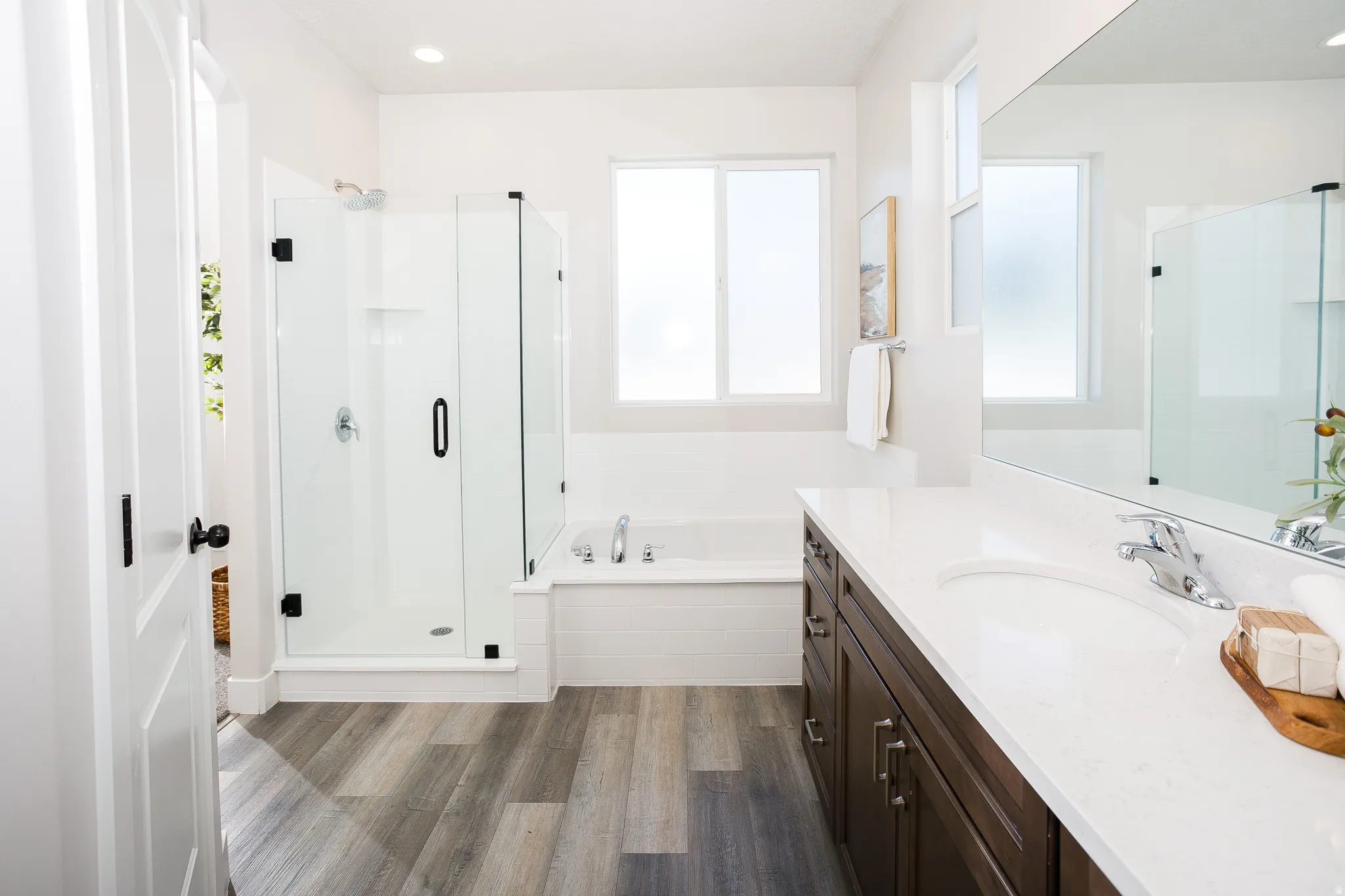 Full bathroom featuring a walk-in shower with a glass enclosure, a built-in bathtub, a double vanity with a stone-finish countertop, and wood-finish flooring