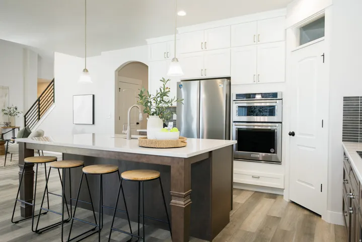 Expansive kitchen island with seating, stainless steel appliances, built-in double ovens, white shaker cabinetry, and wood-finish flooring