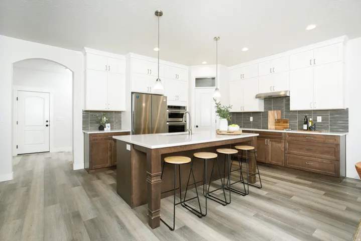 Kitchen featuring an expansive island with seating, stainless steel appliances, two-tone cabinetry, a tile backsplash, and light wood-finish flooring