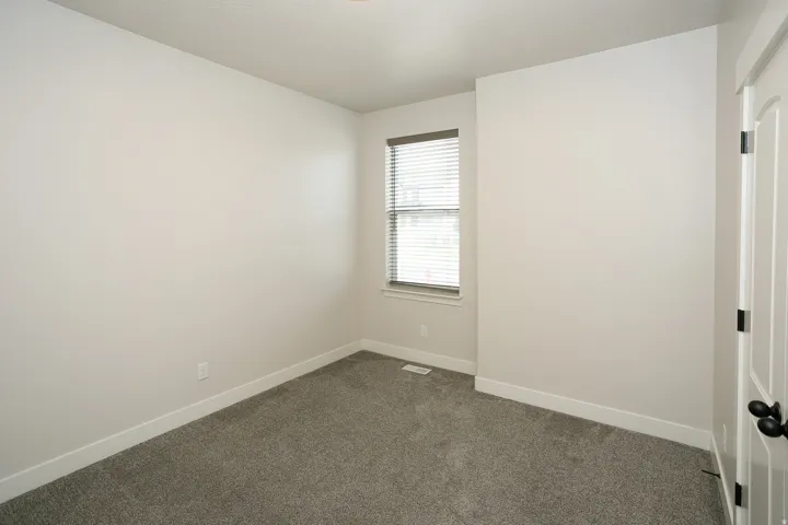 Neutral wall tones, window with horizontal blinds, textured carpet flooring, and a white interior door with black hardware