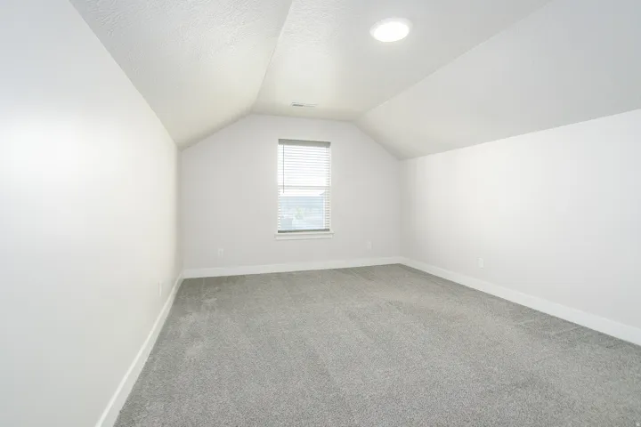 Vaulted ceiling with recessed lighting, gray carpeting, white walls, and a window with blinds