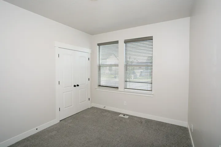 White paneled bi-fold closet doors, carpeted flooring, and two windows with blinds