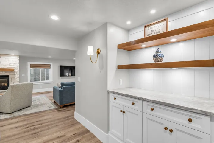 Basement Open-concept living area featuring wood-finish flooring, recessed ceiling lighting, and a custom built-in cabinetry wall with white painted finishes, wood shelving, and brushed bronze hardware