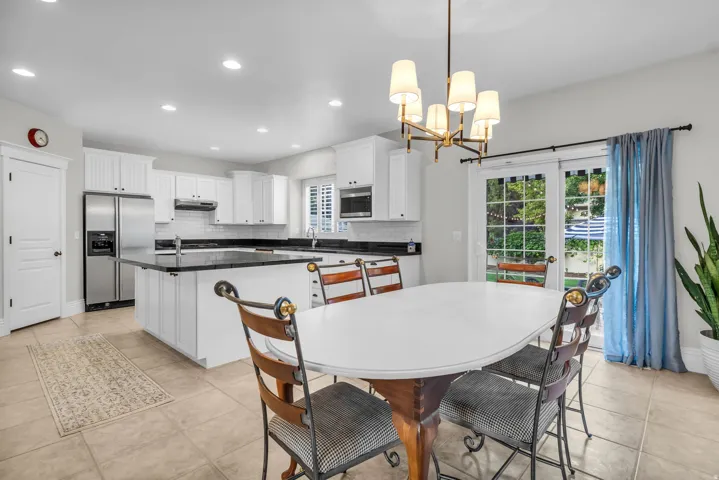 Open-concept kitchen and dining area featuring white cabinetry, stainless steel appliances, black granite countertops, tile flooring, and a pendant light fixture