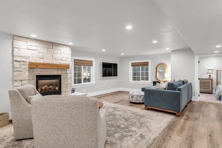 Basement- Spacious open-concept living area featuring fireplace with stone surround and wood mantel, recessed ceiling lighting, wide-plank LVP flooring, and multiple windows