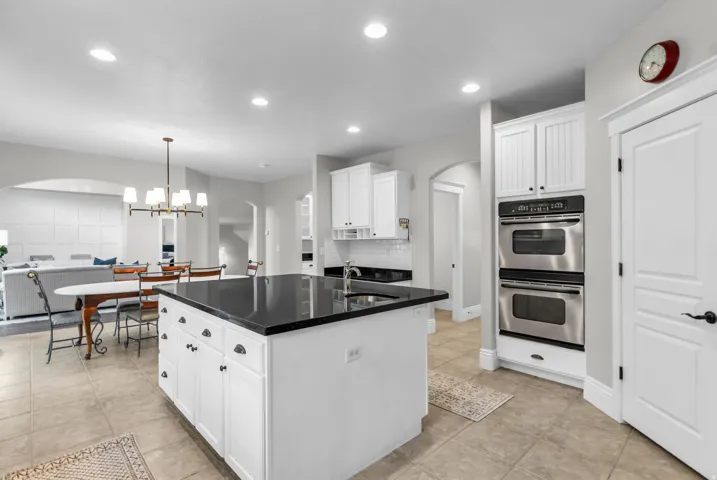 Chef's kitchen featuring a large center island with black stone countertops, white cabinetry, and stainless steel double wall ovens