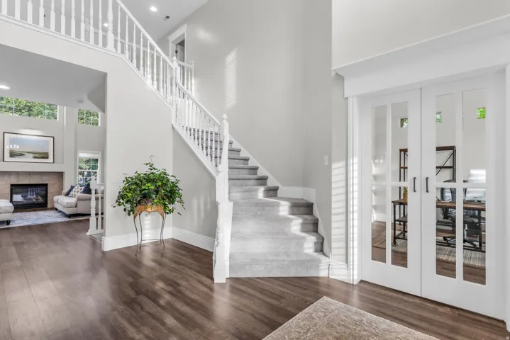 Elegant foyer showcasing a dramatic open staircase with white painted balusters and wood-finish treads, soaring two-story ceilings with recessed lighting, and wide-plank wood-finish flooring throughout