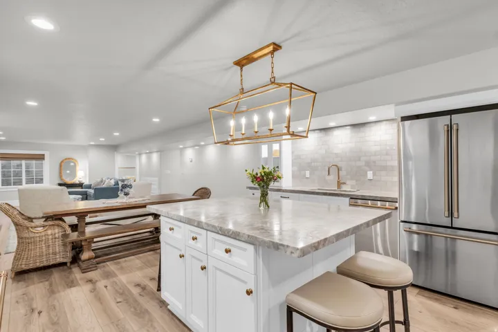 Basement Gourmet kitchen featuring a large island with quartz countertop, white cabinetry with brass hardware, stainless steel appliances, and a statement brass pendant fixture