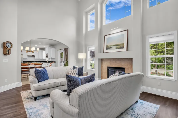 Soaring two-story great room with expansive windows flooding the space with natural light, LVP flooring throughout, and a fireplace with stone surround