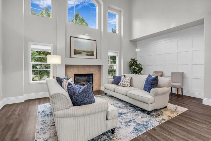 Two-story living area with high ceilings, multiple arched windows, a fireplace with a stone surround, and wood-finish flooring