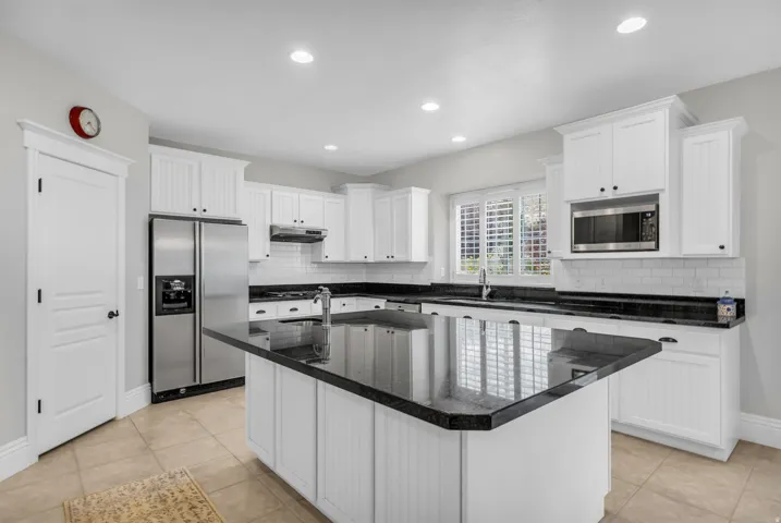 Chef's kitchen featuring white shaker-style cabinetry, black quartz countertops, a large center island with seating, stainless steel appliances including a built-in microwave, and recessed ceiling lighting