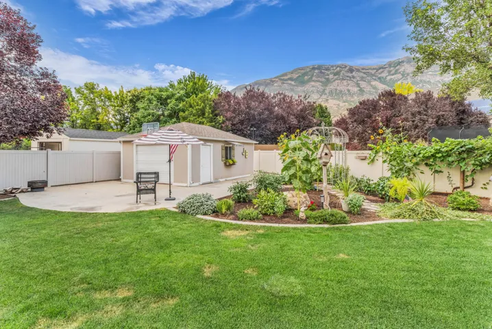 Expansive manicured lawn with mature landscaping and garden beds, backed by mountain views