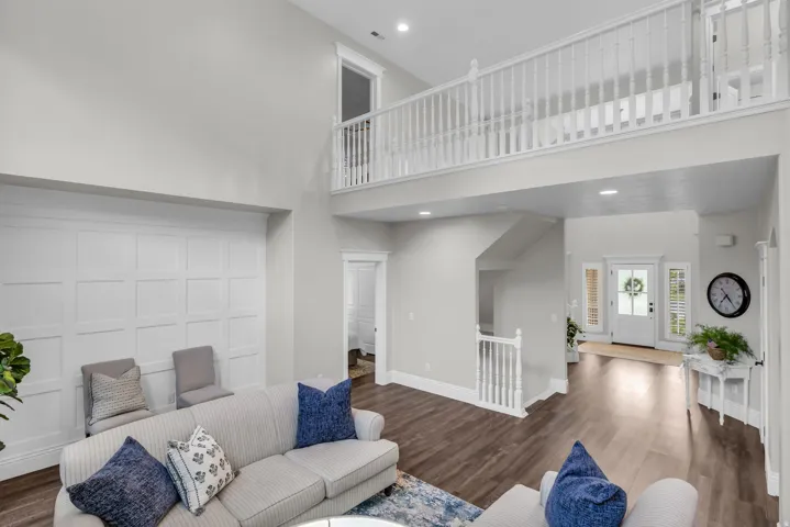 Two-story living area with high ceilings, upper-level railing, wood-finish flooring, and wainscoting paneling