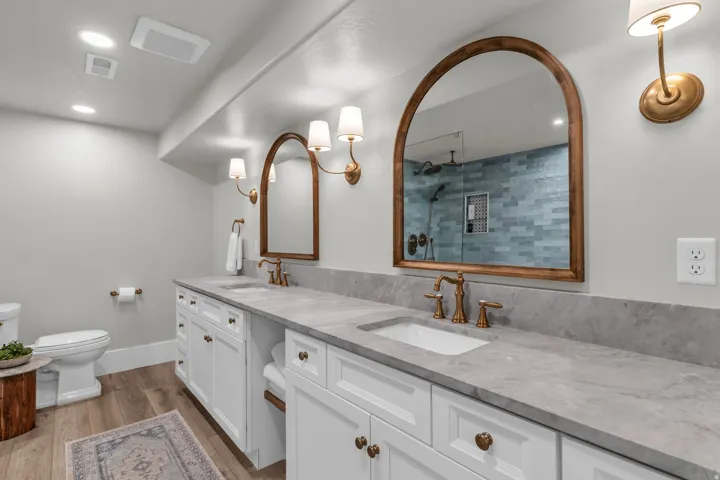 Basement Luxurious primary bathroom featuring dual vanities with marble countertops, bronze-finished faucetry, and arched mirrors