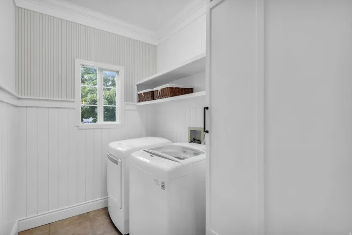 Main Level- laundry room with white shaker-style cabinetry, vertical beadboard wainscoting, and a casement window providing natural light