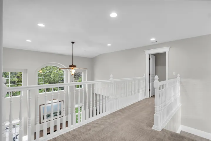 Carpeted hallway with white railing and recessed lighting