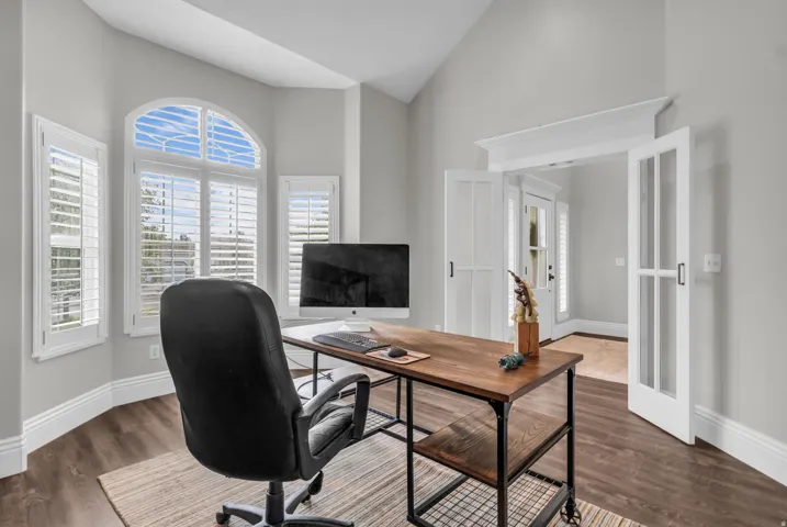 Bay window with plantation shutters, vaulted ceiling, wood-finish flooring, French doors, and substantial white trim