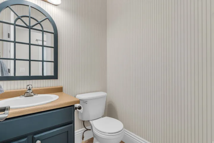 Half Bath Main Level- Pedestal sink with chrome faucet, built-in vanity with cabinetry, and an arched mirror with grid detailing
