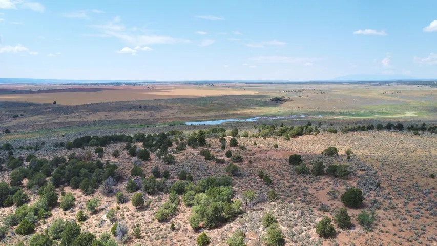 Expansive high desert landscape featuring a natural water body, diverse scrub vegetation, and distant mountain ranges under a vast sky