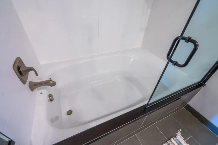 Spa-inspired primary bathroom featuring a soaking tub with integrated jets, brushed nickel fixtures, white subway tile surround, and dark tile flooring