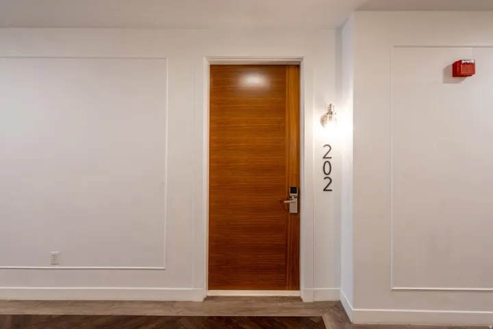 Wood-finish entry door with modern hardware, illuminated by a wall-mounted sconce