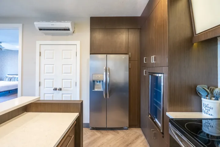 Stainless steel refrigerator, integrated beverage cooler, rich wood-finish cabinetry, light-toned countertop, and wood-finish flooring