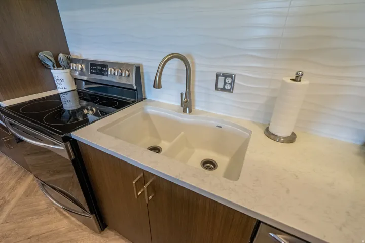 Modern kitchen featuring a dual-basin undermount sink with brushed nickel gooseneck faucet, light quartz countertops, wood-finish cabinetry, stainless steel appliances including a slide-in range, and subway tile backsplash